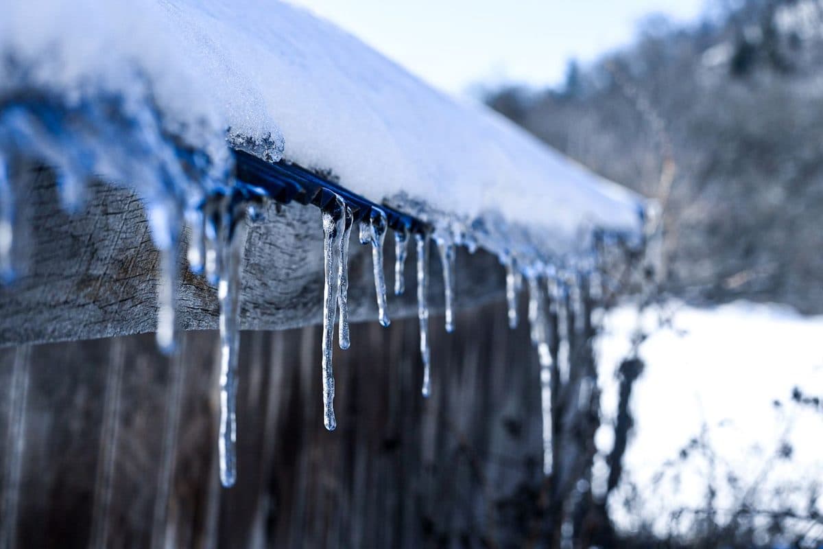 Icicles hanging from the edge of a snow-covered roof, the visible sign of freeze danger for North Texas homes
