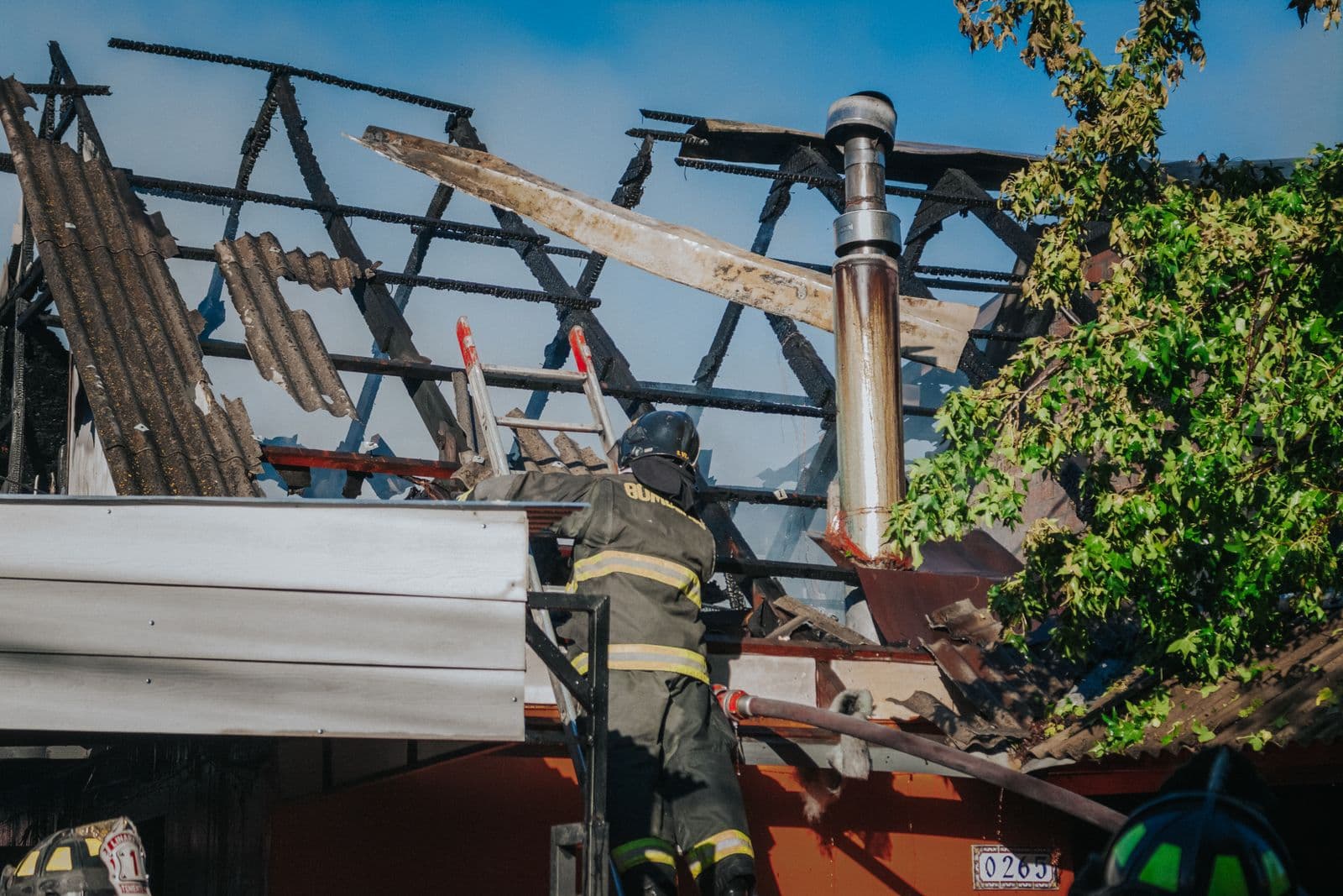 Firefighter clearing debris from a burned roof after a house fire, showing the aftermath that requires professional fire and smoke damage restoration