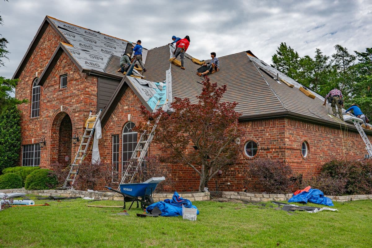 Roofers working on a brick home in Allen, Texas, addressing damaged shingles and roofing materials after a severe storm