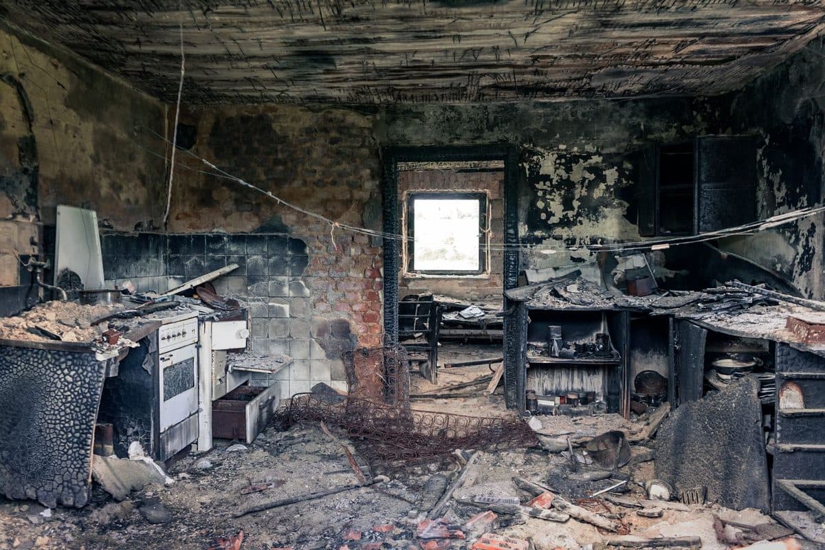 A kitchen interior blackened with soot and smoke residue after a house fire, the kind of embedded residue that keeps releasing odor long after the fire is out