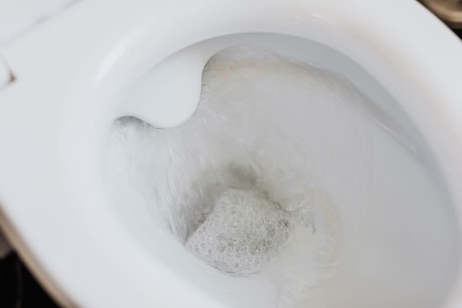 Close-up of a white toilet bowl with water churning and foaming at the drain during a clogged flush