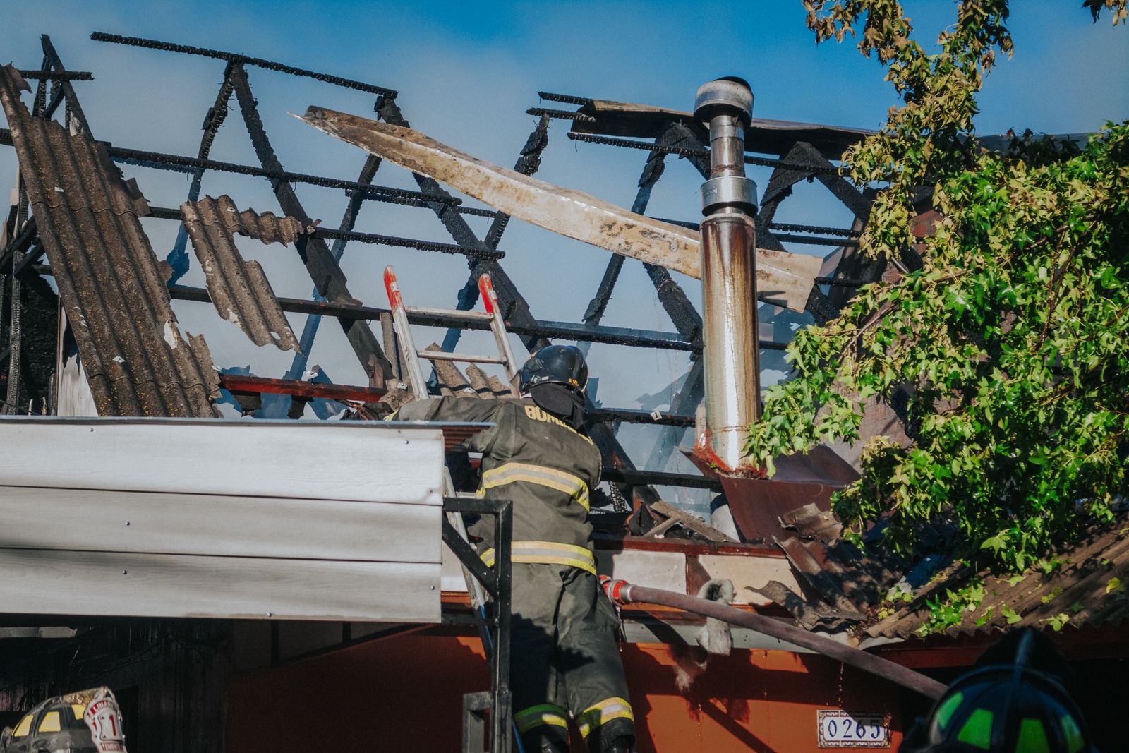 Firefighter clearing debris from a burned roof after a house fire, showing the aftermath that requires professional fire and smoke damage restoration