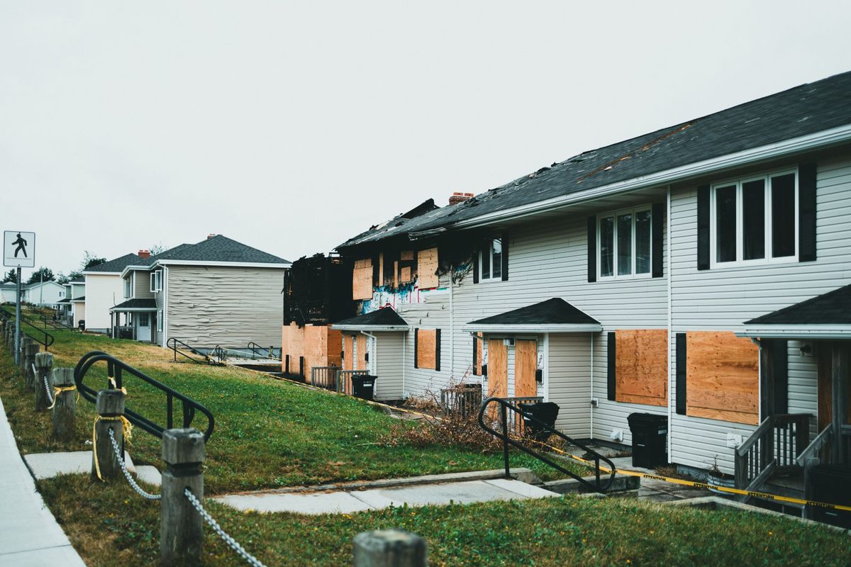 Plywood board-up on fire-damaged homes with a charred roofline, the protection step that comes before any restoration work