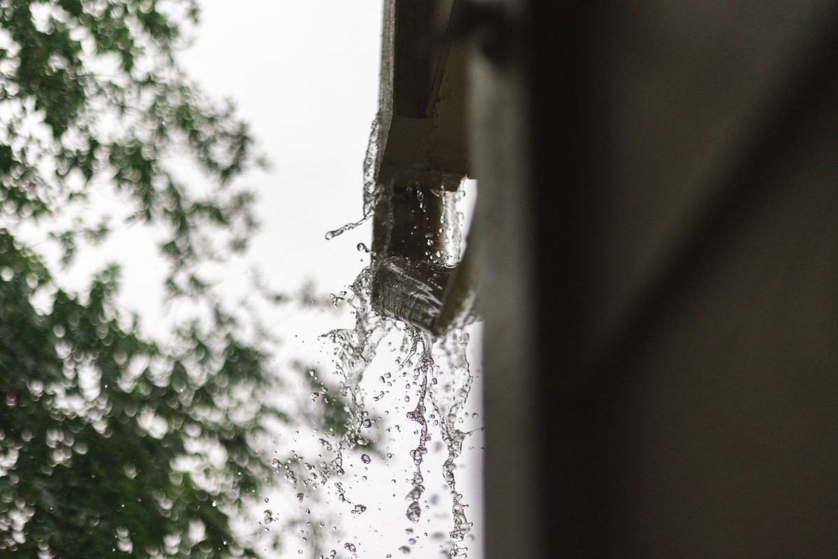 Rainwater pouring over the end of a home gutter and falling against the wall, the kind of exterior drainage failure that feeds clay soil moisture into a North Texas slab