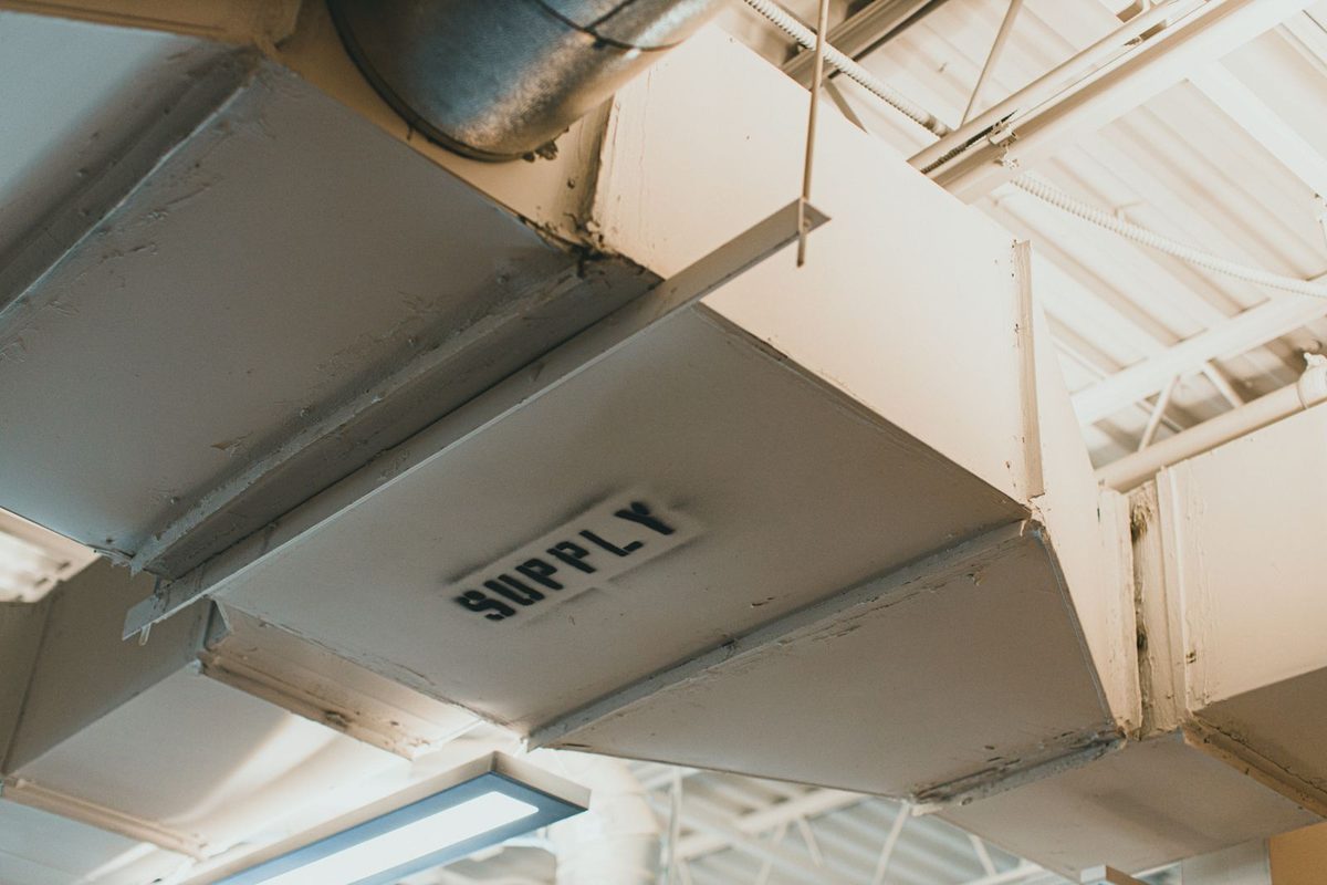 A metal HVAC supply air duct with visible grime along the seams, the path smoke odor travels back into every room